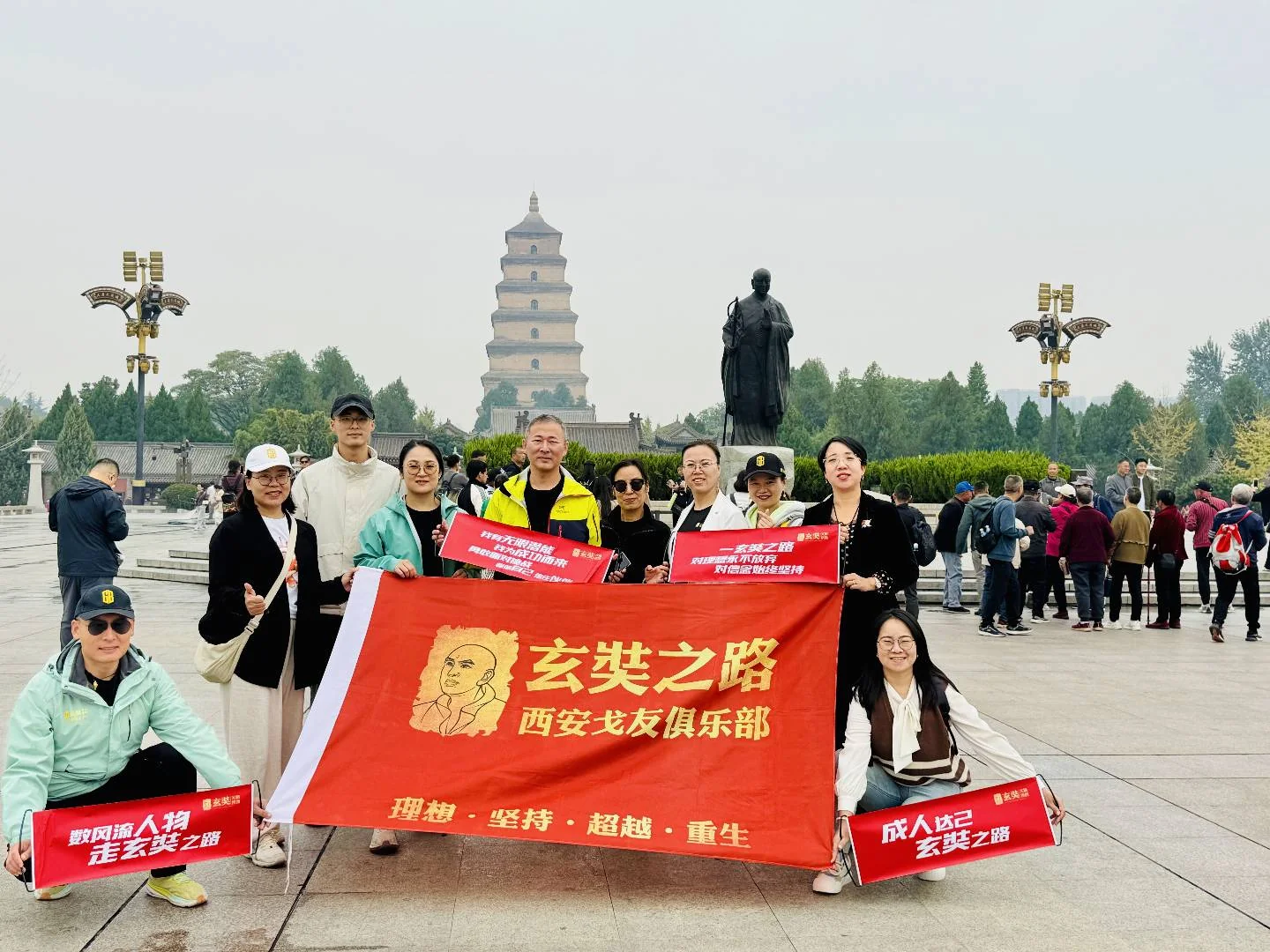 塔与人物雕像前的团队合影，横幅写有玄奘之路西安戈友俱乐部